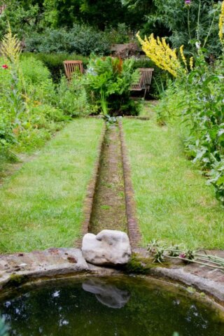 Een open goot die leidt naar een vijver in een weelderige tuin.